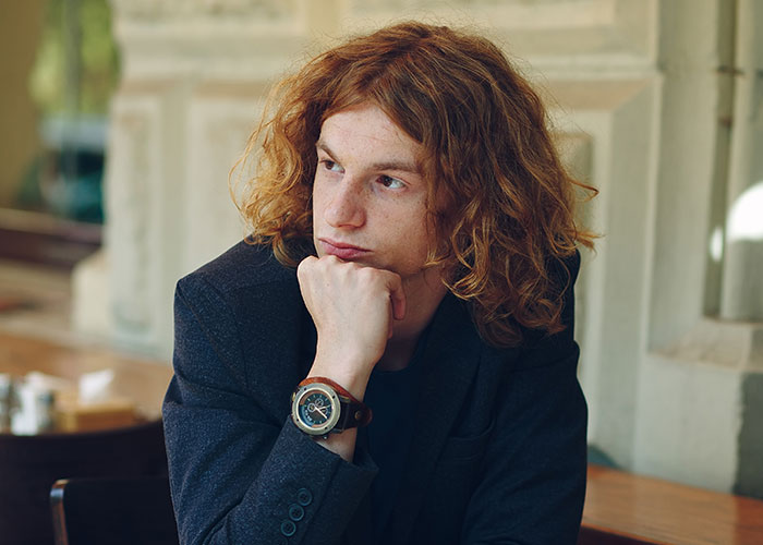 Young man with curly red hair wearing a dark jacket, looking thoughtful, symbolizing moving away and changing identity.