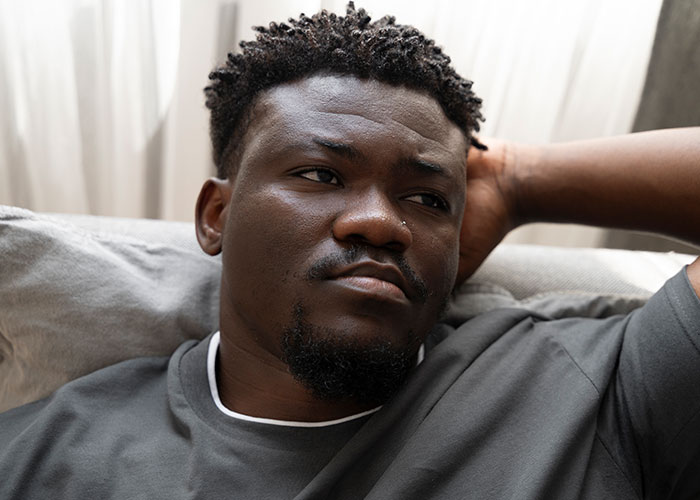 Thoughtful man lying on a couch, reflecting on life changes and moving away to rewrite his story.