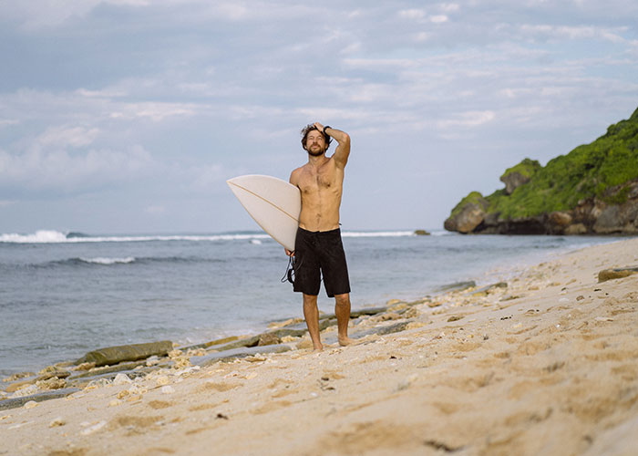 Man standing on beach holding surfboard, symbolizing life change and people rewriting their life story.