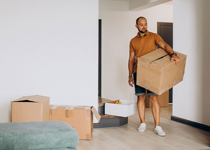 Man carrying a moving box inside a home, illustrating the concept of moved away and changing life story.