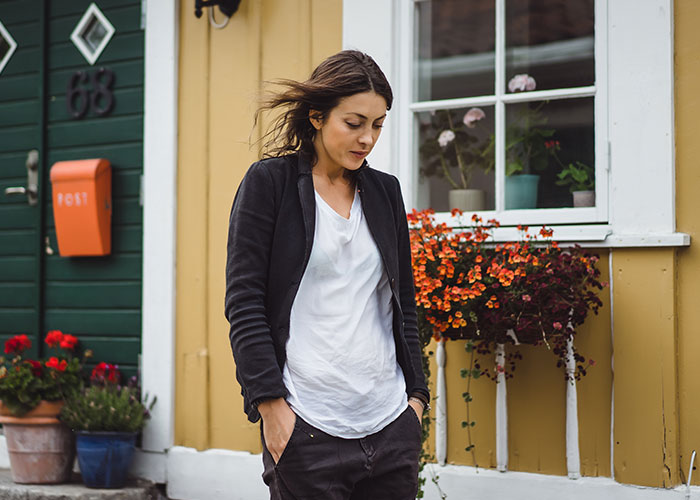 Young woman standing outside a house with flowers, reflecting on moved away and changed name for new life story.