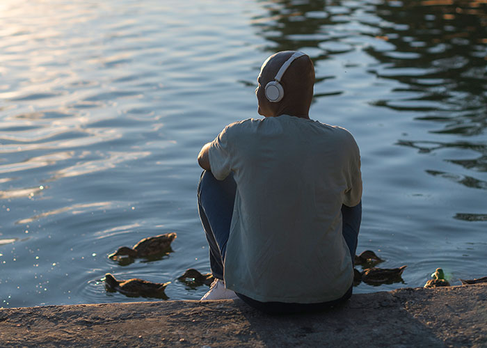 Person wearing headphones sitting by water with ducks, symbolizing moving away and changing life story.