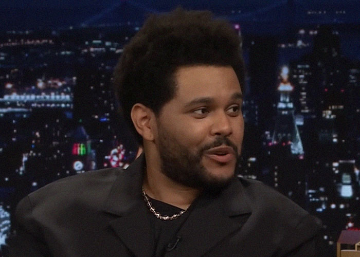 Man in a black jacket and chain necklace speaking during a late-night talk show about people who moved away and changed their name.