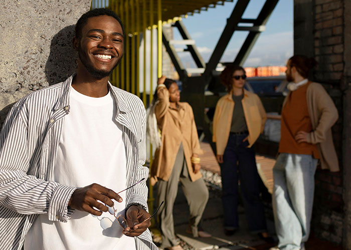 Young man smiling confidently holding sunglasses, with friends in the background symbolizing life change and moving away.