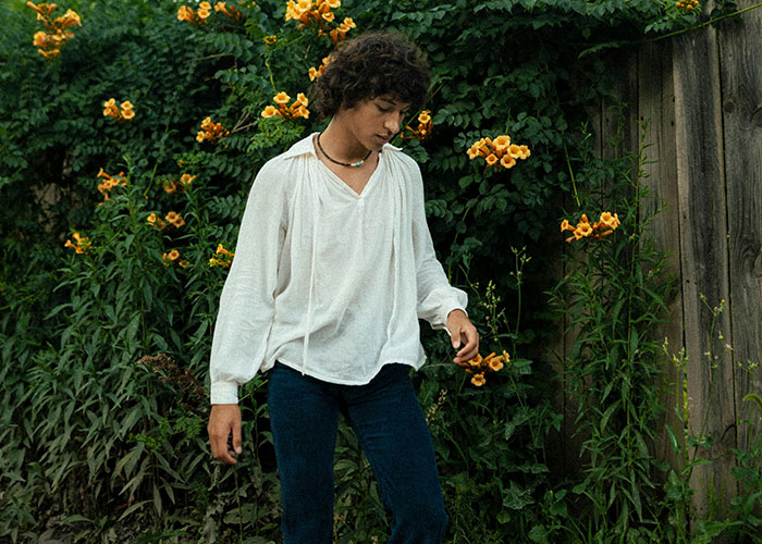 Young person in a white shirt walking near flowering plants, symbolizing moving away and changing identity.