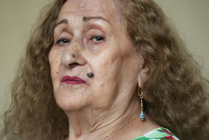 Elderly woman with curly hair and colorful earrings, reflecting on stepdaughter and ex-wife family conflict issues.