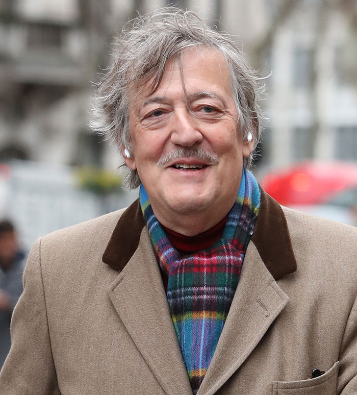 Stephen Fry outdoors wearing a beige coat and colorful scarf, associated with Stephen Fry gives brutal takedown of J.K. Rowling.