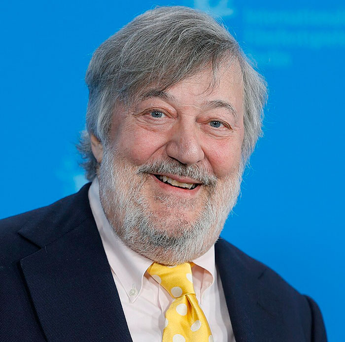 Stephen Fry smiling in a suit and yellow tie, known for giving a brutal takedown of J.K. Rowling.