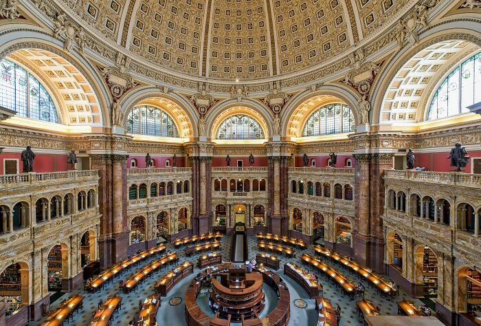 Grand interior of a stunning and impressive library with ornate architecture, large dome, and rows of reading desks lit by warm lights.