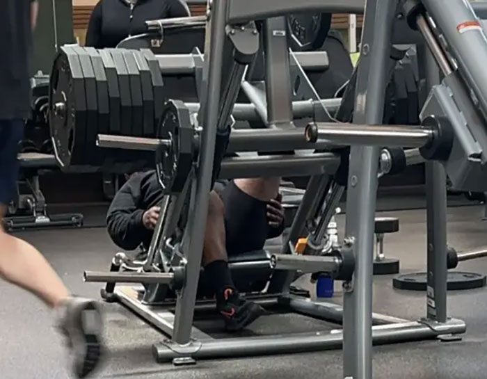 Person struggling with heavy weights on gym machine, illustrating annoying gym moments during workout session.