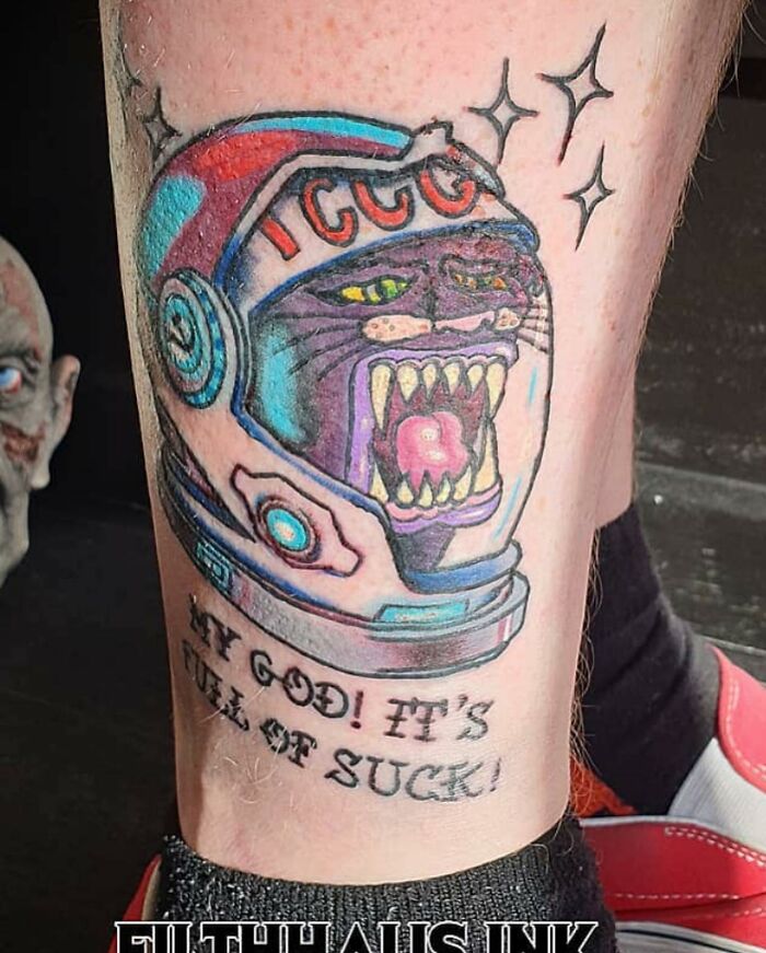Tattoo of a fierce cat in a space helmet with text expressing frustration, showcasing bizarre choices in tattoos.