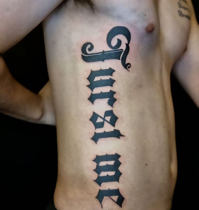 Vertical black tattoo reading evolved in gothic font on a person's bare side showcasing bizarre tattoo choices.