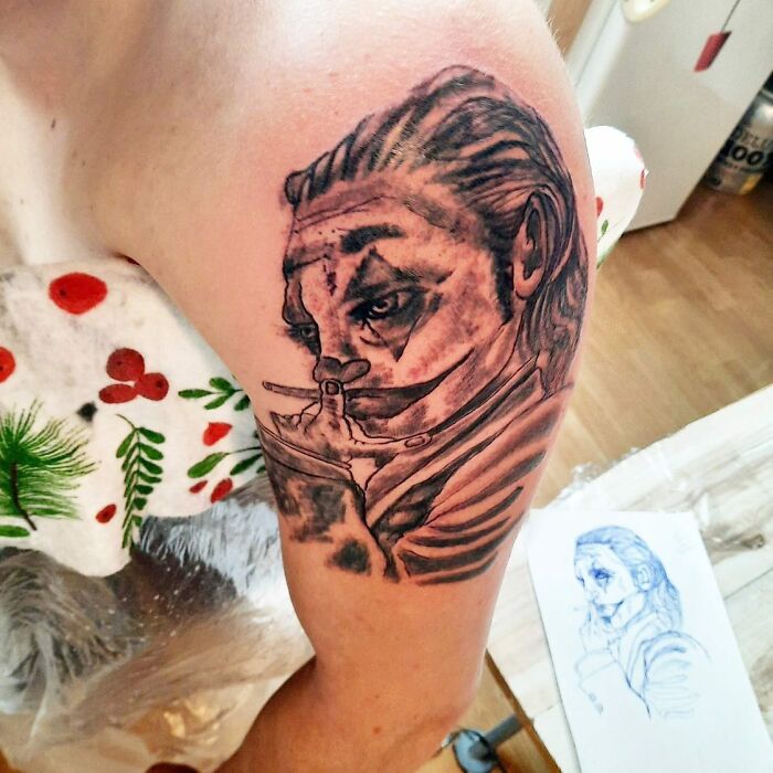 Realistic black and grey tattoo of a man with face paint on a person's upper arm, showcasing bizarre tattoo choices.