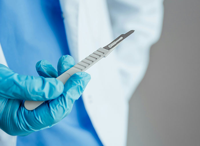 Surgeon wearing blue gloves holding a surgical scalpel, preparing for a procedure related to the human body facts.