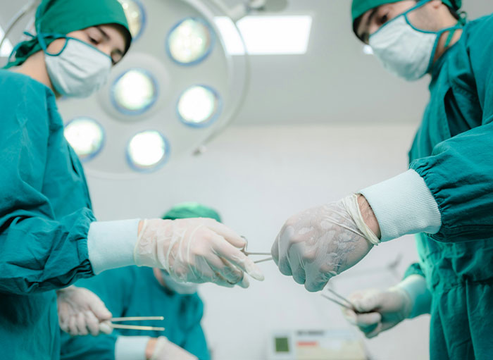 Surgeons in green scrubs and masks perform a precise medical procedure in a well-lit operating room setting.