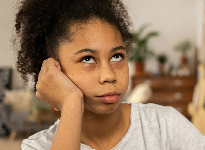Young woman with curly hair looking up thoughtfully, illustrating curiosity about weird facts of the human body.