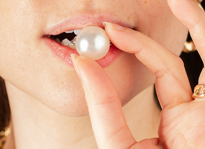 Close-up of a person holding a pearl earring near lips, illustrating weird facts about the human body shared by surgeons.