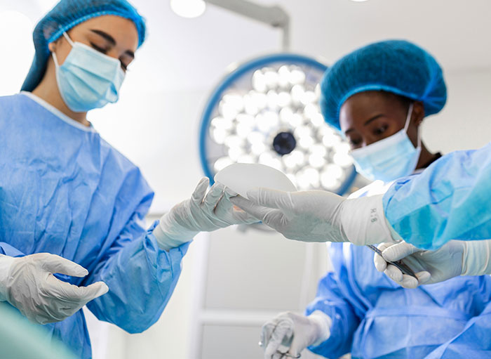 Two surgeons in blue scrubs and masks handling surgical tools in an operating room focused on the human body.