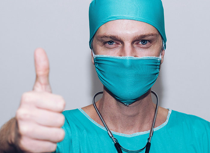 Surgeon wearing teal scrubs and mask giving thumbs up, representing weird facts about the human body shared by surgeons.
