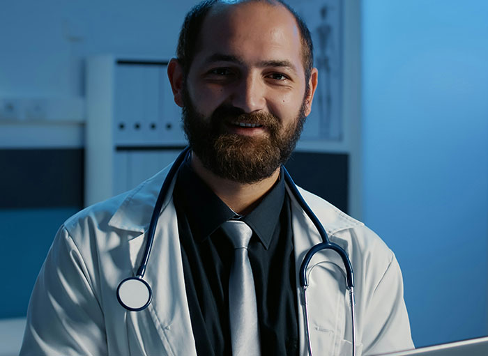 Smiling male surgeon with a beard wearing a white coat and stethoscope sharing weirdest facts about the human body