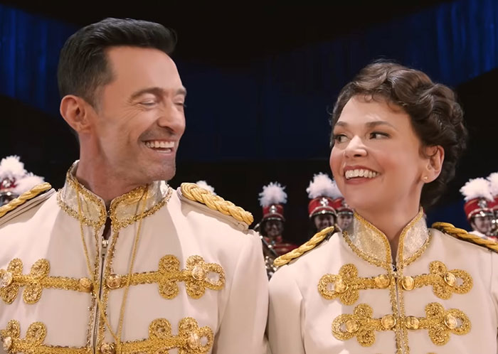 Hugh Jackman and Sutton Foster smiling together in matching white and gold costumes during a musical performance. Hugh Jackman and Sutton Foster smiling together in matching white and gold costumes during a musical performance.