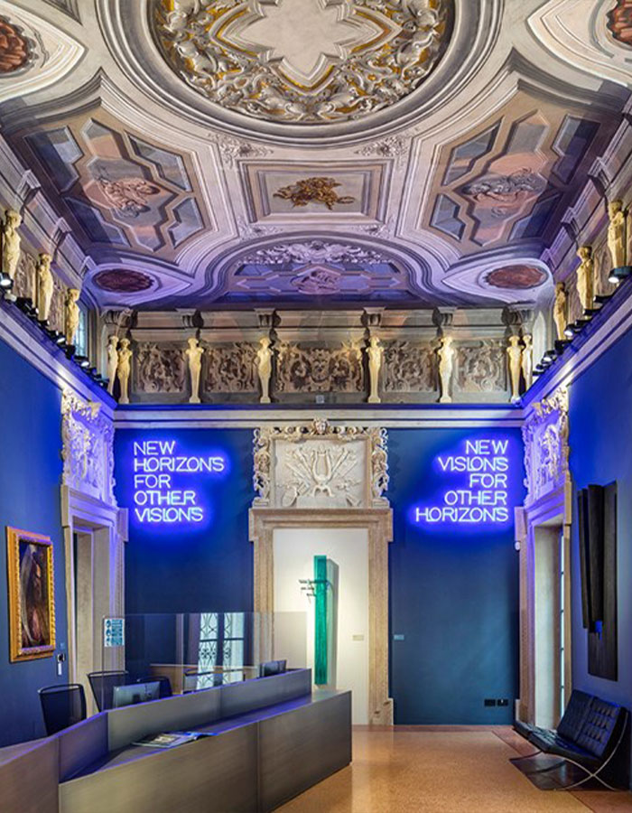 Tourist inside Italian gallery with ornate ceiling and neon signs in blue, related to Van Gogh chair exhibit.