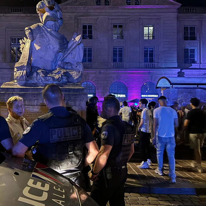 Police officers monitoring a crowd at night near a statue at a busy music festival addressing violence against women concerns.
