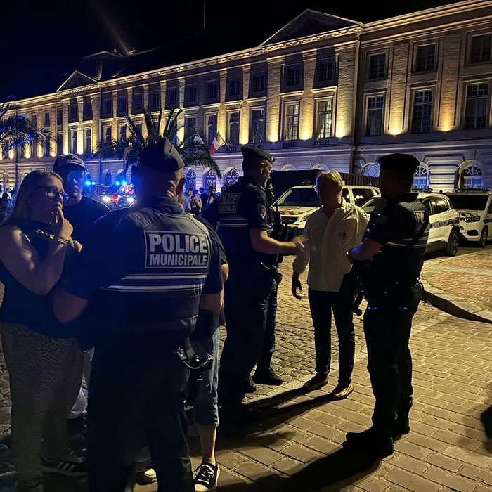 Police officers speaking with people at night outside a large building after syringe jabbing violence against women incident.