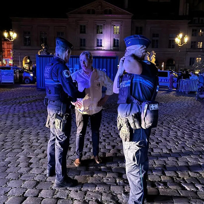 Police officers speaking with a man at night after reports of violence against women and syringe attacks at a music festival.