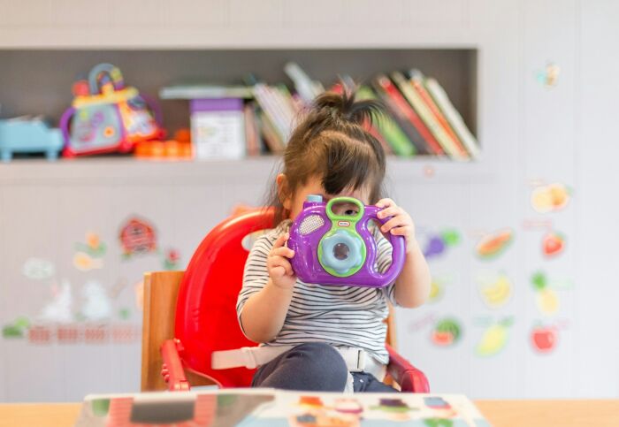Toddler sitting in a high chair holding a toy camera, illustrating millennials and industries that took a huge hit.