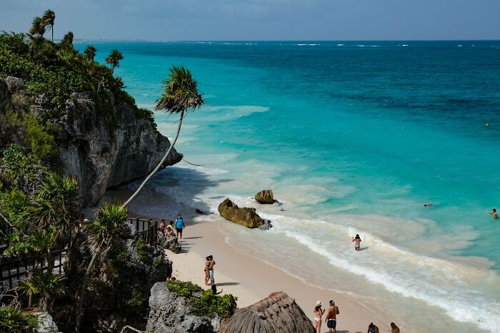 Tropical beach with turquoise water and tourists, illustrating travel destinations tourists advise to avoid.