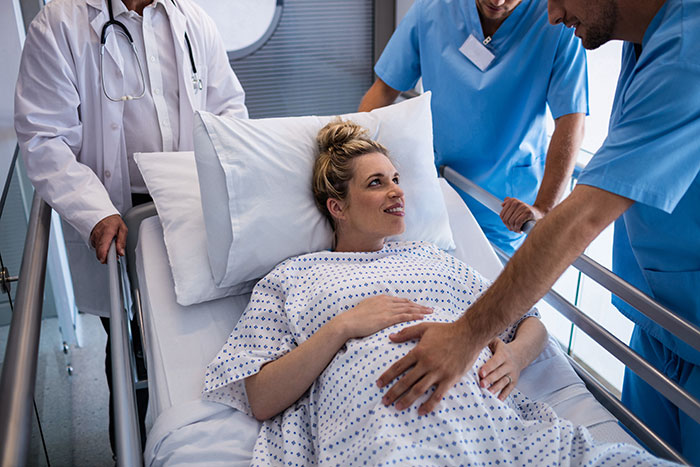 Pregnant woman in a hospital bed surrounded by medical staff preparing for delivery, highlighting delivery room tensions.