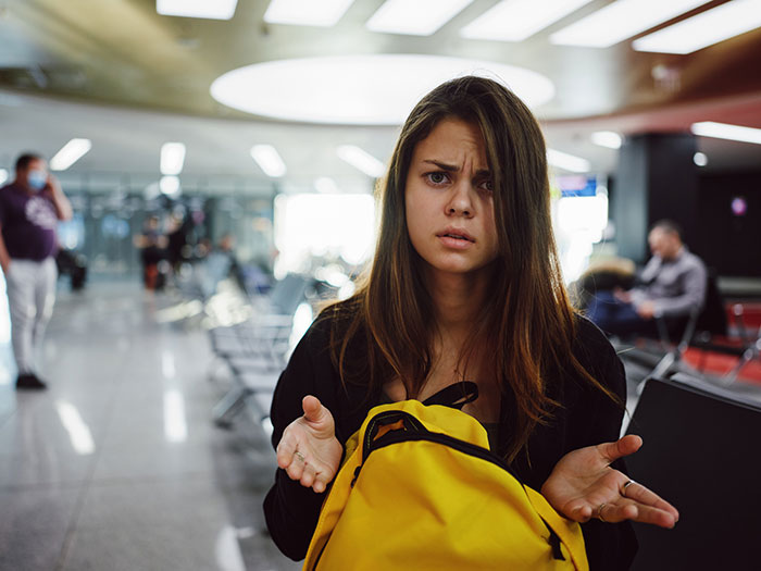 Frustrated teenage girl with yellow backpack at airport, representing family vacation turns sour over business class upgrade issue. Frustrated teenage girl with yellow backpack at airport, representing family vacation turns sour over business class upgrade issue.