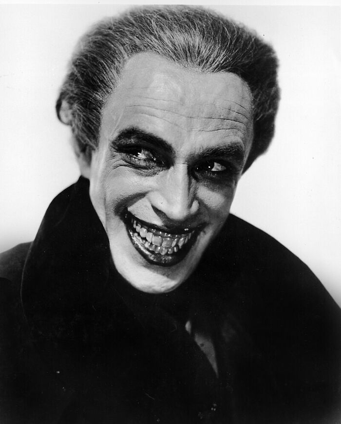Black and white photo of an unsettling man with creepy makeup and a sinister smile from the past.