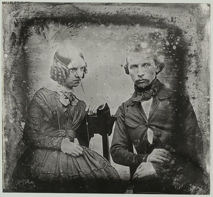 Creepy and unsettling old photo of a Victorian-era couple with serious expressions sitting close together.