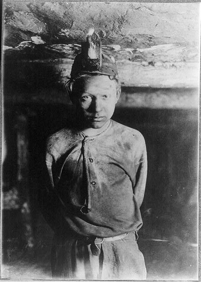 Black and white photo of a man with his hands tied behind him wearing a miner's helmet in a dark, creepy setting.