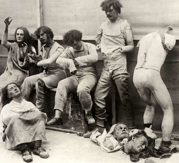 Creepy and unsettling vintage photo showing five distressed people in tattered clothes with dismembered mannequin parts on the floor.