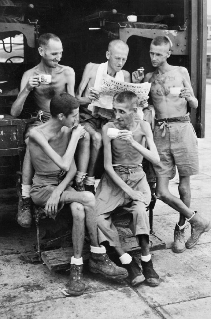 Emaciated men in a historic black and white photo, appearing incredibly creepy and unsettling while sharing tea and reading.