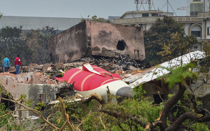 Wreckage of a plane crash site with debris and burnt structures as investigators survey the area after the accident.