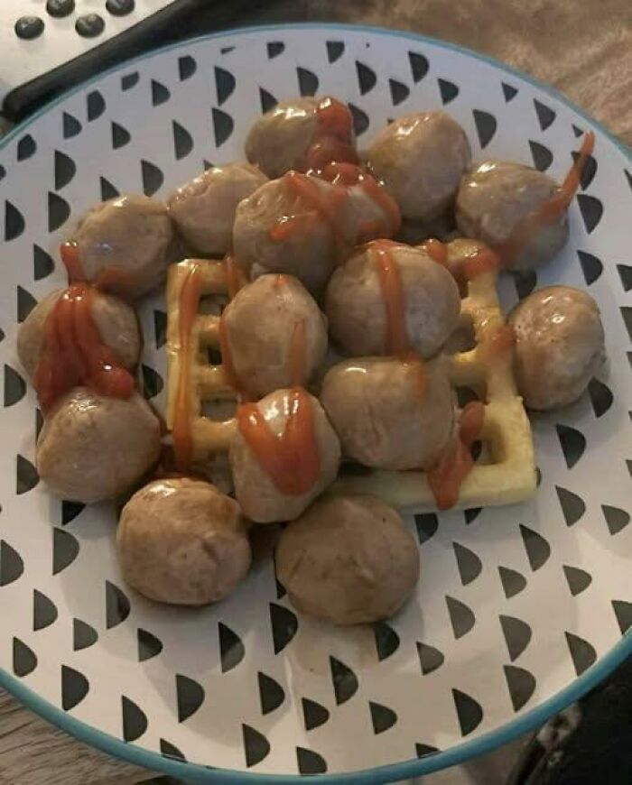 Plate of meatballs with waffle underneath and drizzled with ketchup, an example of disgusting food pics that might ruin appetite.