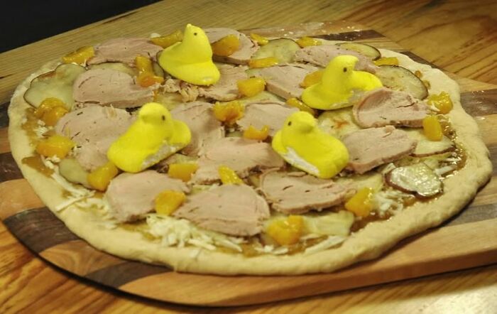Pizza topped with sliced turkey, pickles, orange bits, and yellow marshmallow chicks creating a disgusting food visual.