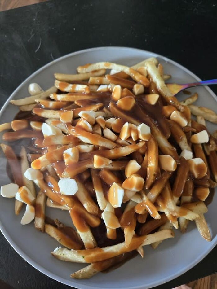 Plate of fries covered in melted cheese curds and brown gravy, a classic but messy dish in disgusting food pics.