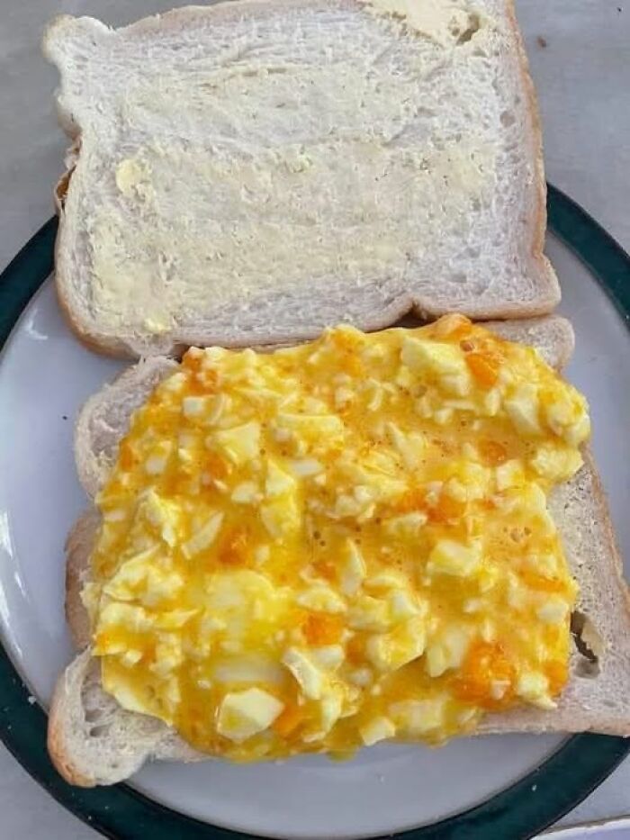 Close-up of a sandwich with chunky, unappetizing egg salad on white bread, an example of disgusting food pics.