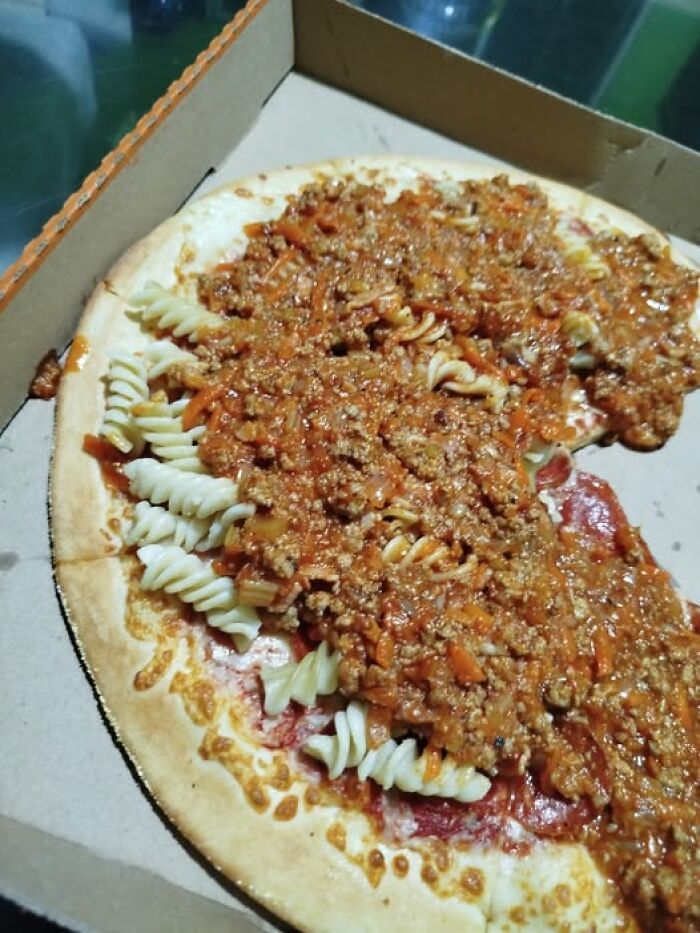 Pizza topped with cooked rotini pasta and a thick meat sauce, an unusual and unappetizing food combination.