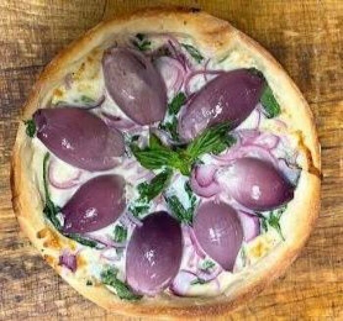 Pizza topped with whole cooked purple onions and greens on a wooden surface, an example of disgusting food pics.