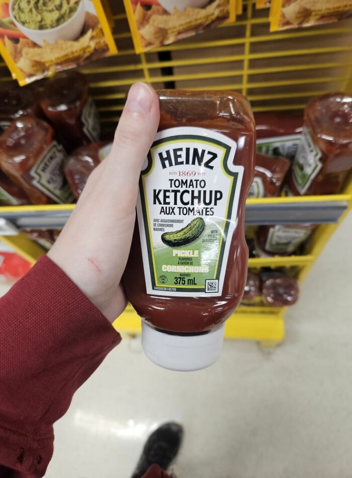 Hand holding a bottle of Heinz tomato ketchup with pickle flavoring in a grocery store, unusual food product packaging.