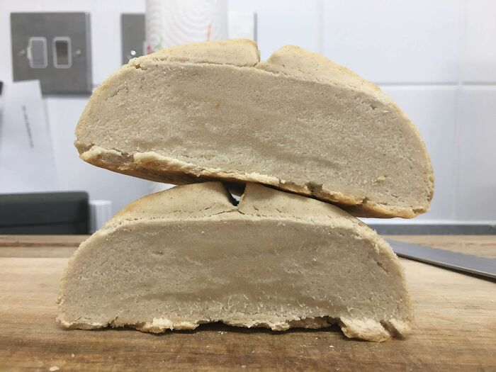 Close-up of two beige, dense, moldy food pieces stacked on a wooden surface in disgusting food pics.
