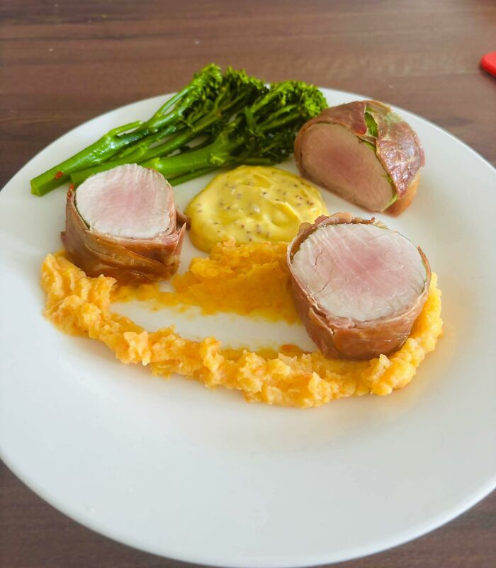 Plate with three pieces of undercooked meat, mashed orange vegetables, mustard sauce, and green broccoli, a disgusting food pic.