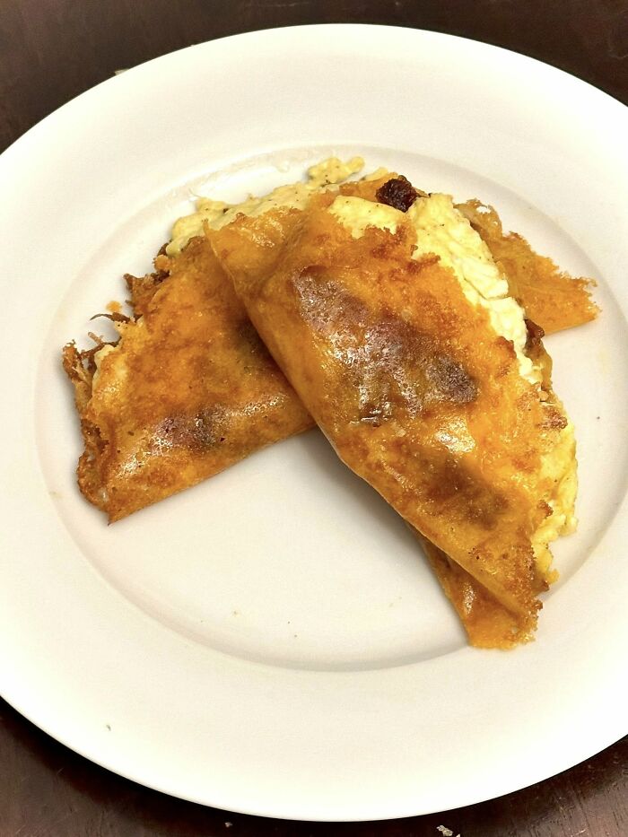 Two overcooked and greasy folded omelets on a white plate, fitting the disgusting food pics keyword.