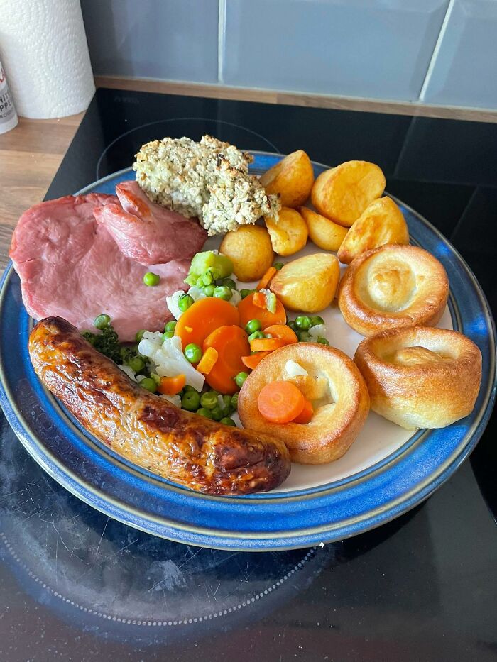 Plate of food with cooked sausage, ham, roasted potatoes, mixed vegetables, and Yorkshire puddings in a disgusting food pic.